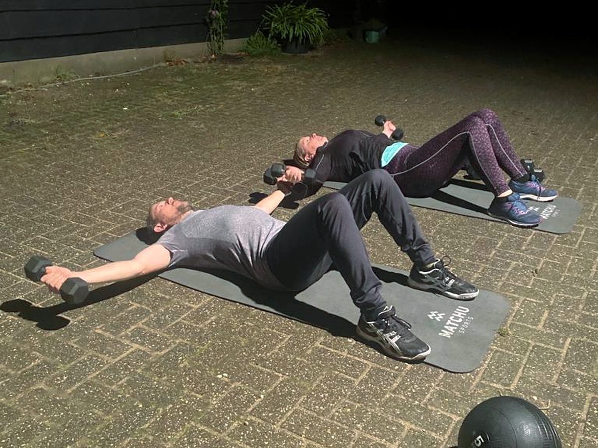Drie mensen liggen naast elkaar op matten en doen een oefening met gewichten